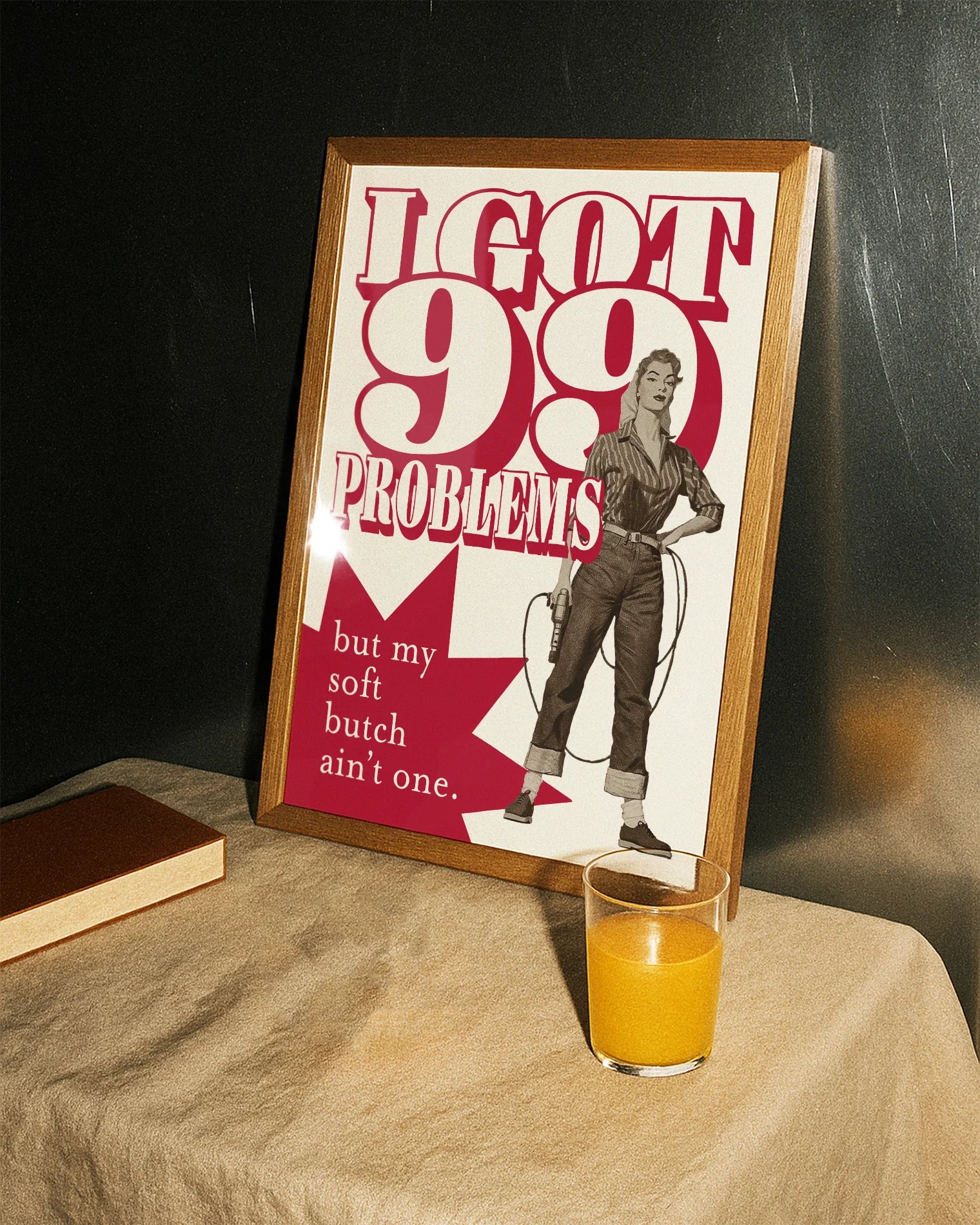 A framed poster depicting a soft butch wearing jeans and a shirt, holding a drill with the text: “I GOT 99 PROBLEMS” and “but my soft butch ain't one.”