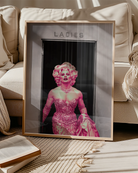 A poster with a muscular drag queen in a sparkling dress, full makeup, and wig, confidently strutting out of the ladies’ room.