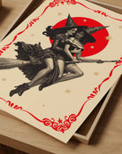 A poster featuring two lesbian witches flying on a broomstick through the night. They share a romantic gaze, surrounded by stars and a large red full moon.
