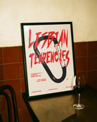 A print with an illustrated carabiner, with the text 'Lesbian Tendencies' in red.