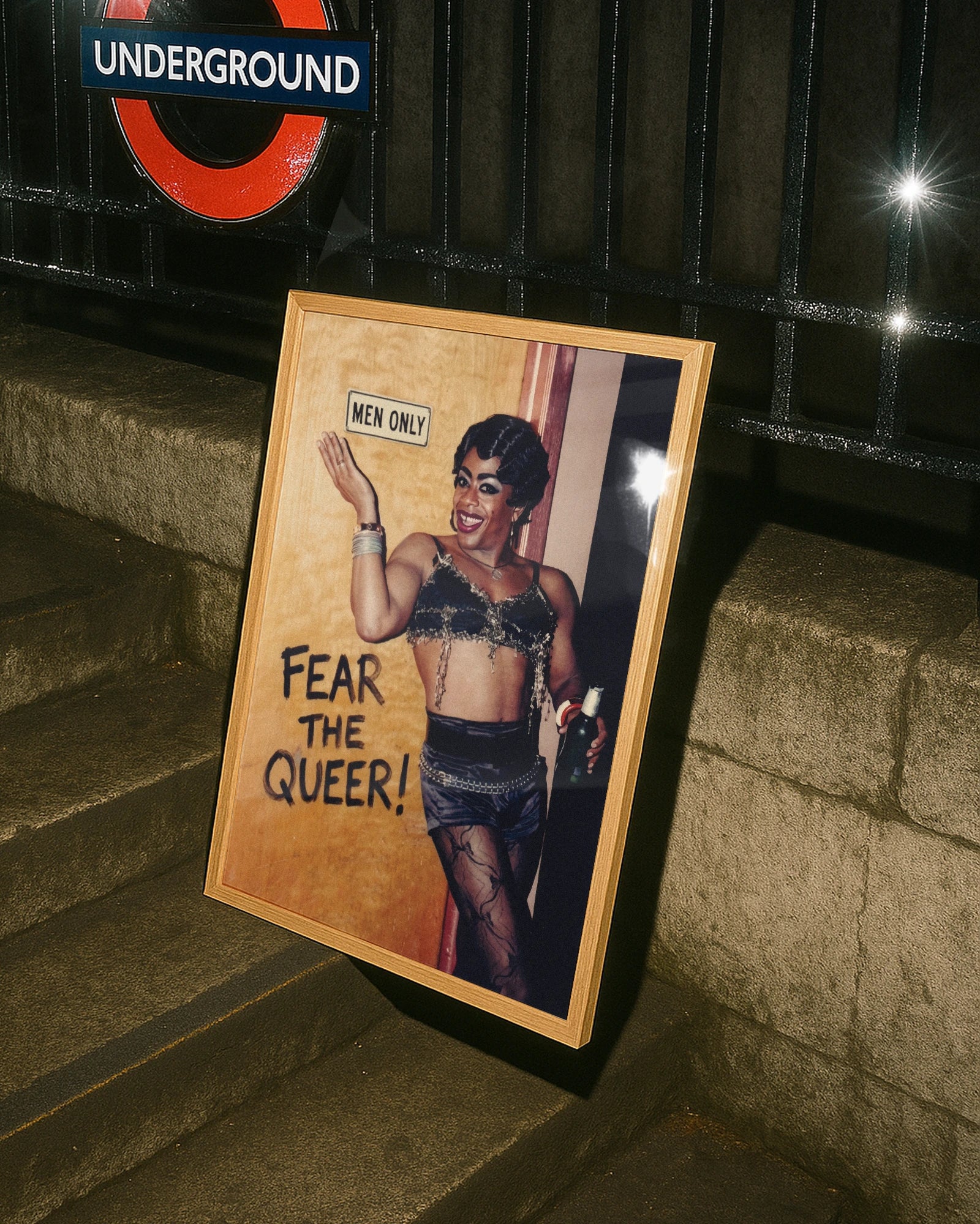 A framed poster with a black drag queen standing in front of a wall with a sign 'MEN ONLY', smiling.