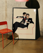 A poster with two fine looking gentleman in suits, cuddling on a couch. Vintage, 60's and elegant style.