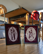 A print with two illustrated lesbian cowgirls in a loving, playful pose.