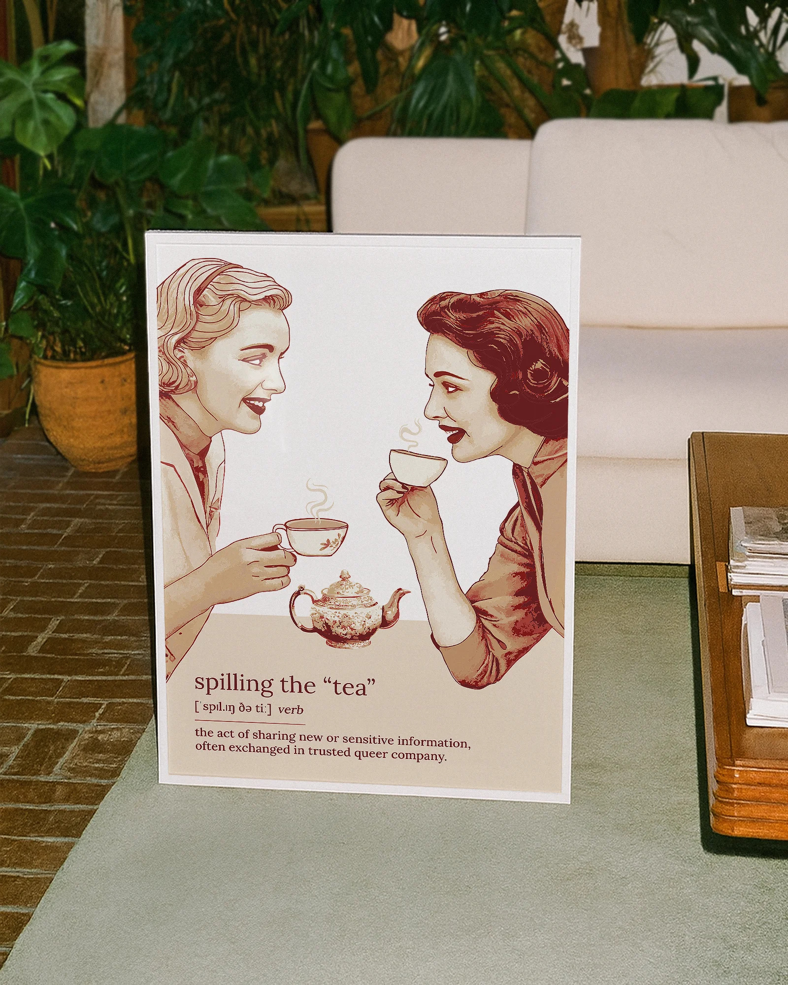 A framed poster featuring two women gossiping over tea, accompanied by the text: “Spilling The Tea – Verb – The act of sharing new or sensitive information, often exchanged in trusted queer company.”