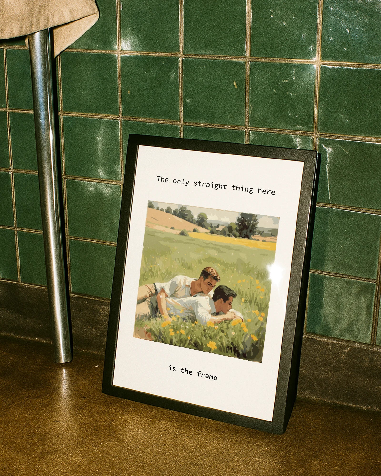A poster with two gay men cuddling together in a summery green field of yellow flowers, with the text: “The only thing straight here is the frame.”