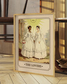 A print with an illustrated, sapphic, newlywed couple in a tarot card style with the text 'The Lovers'.