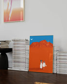 A framed print with a brides couple in white dresses walking hand in hand in a desert.