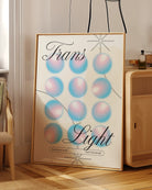 A print with the text 'Trans Light', against a background with gradient circles in the transgender flag colours.