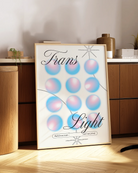 A print with the text 'Trans Light', against a background with gradient circles in the transgender flag colours.
