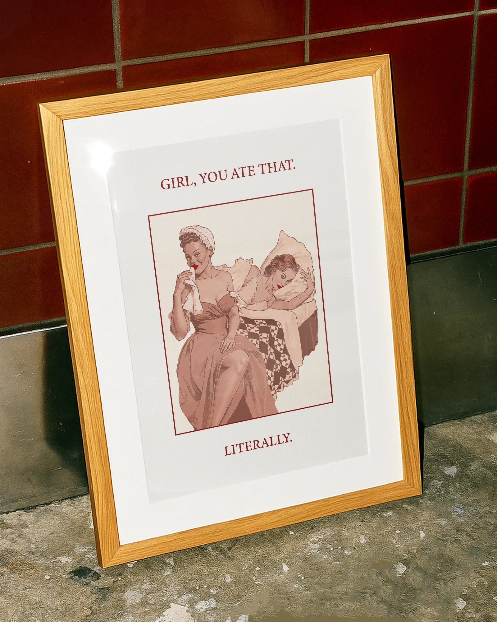 A poster featuring a woman wiping her mouth with a cloth napkin while sitting on the edge of a bed, with another woman lying behind her. Text on the artwork reads: “GIRL, YOU ATE THAT. LITERALLY.”
