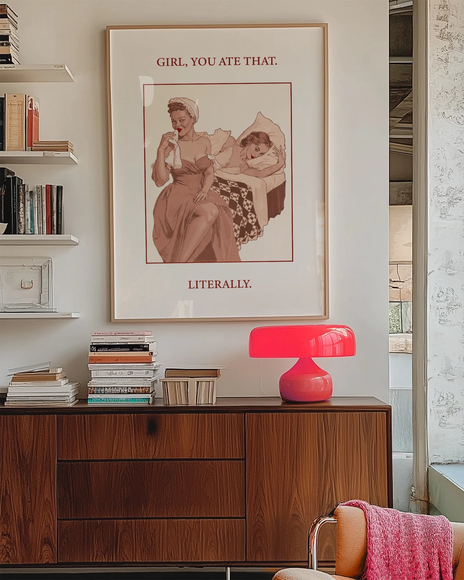 A poster featuring a woman wiping her mouth with a cloth napkin while sitting on the edge of a bed, with another woman lying behind her. Text on the artwork reads: “GIRL, YOU ATE THAT. LITERALLY.”