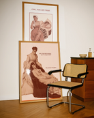 A framed poster featuring two sapphic women from the Victorian era in a conversation: 'Am I the first woman you've slept with?' 'You mean tonight?'.