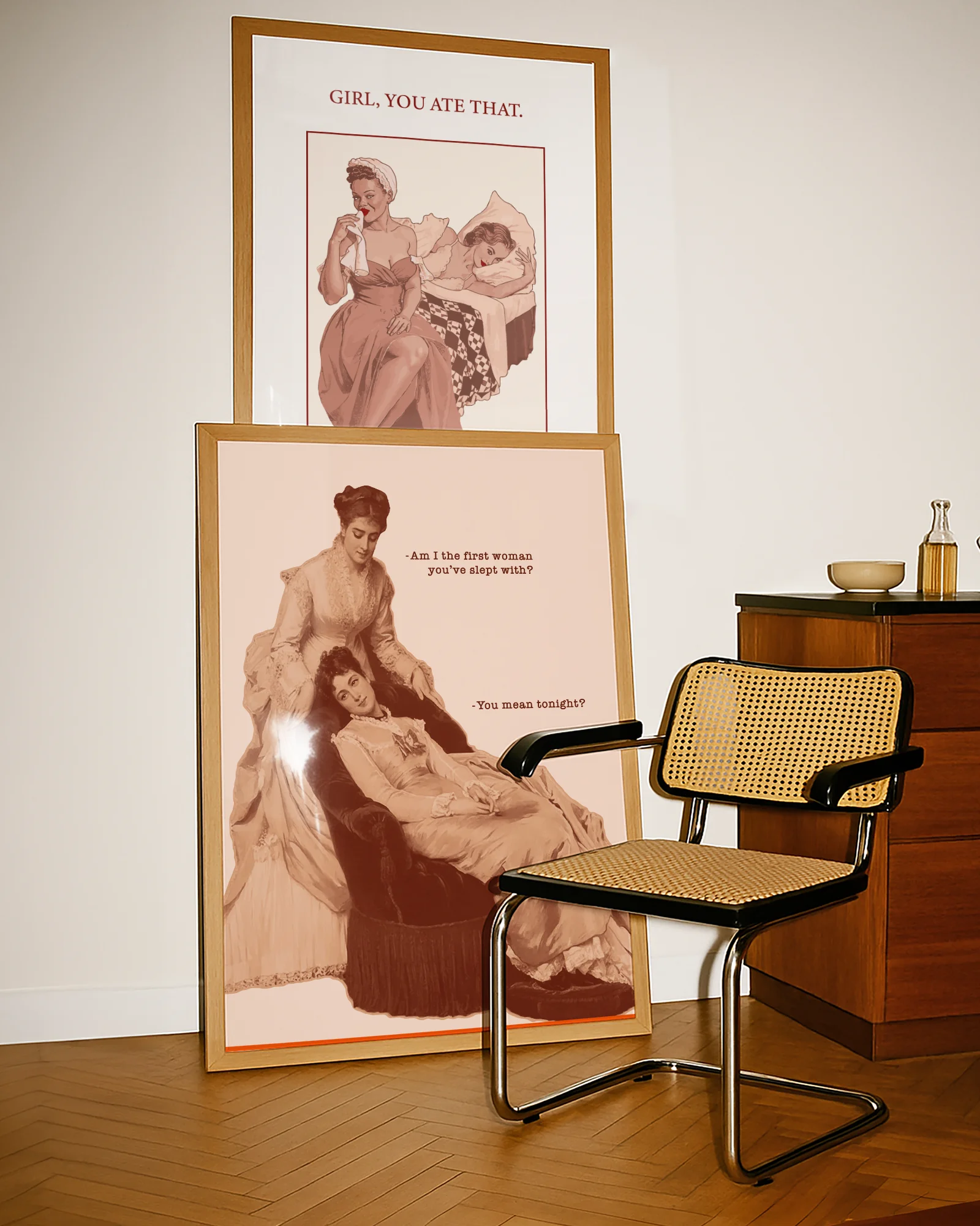 A framed poster featuring two sapphic women from the Victorian era in a conversation: 'Am I the first woman you've slept with?' 'You mean tonight?'.