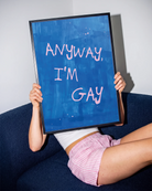 A poster with the text 'ANYWAY, I'M GAY' in pink, against a blue abstract background.