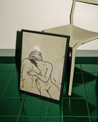 A framed print with two, naked women holding each other in a green field.