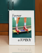 A framed print with a girl in red high heels standing on a skateboard, with the text: 'Forever a TOMBOY'.