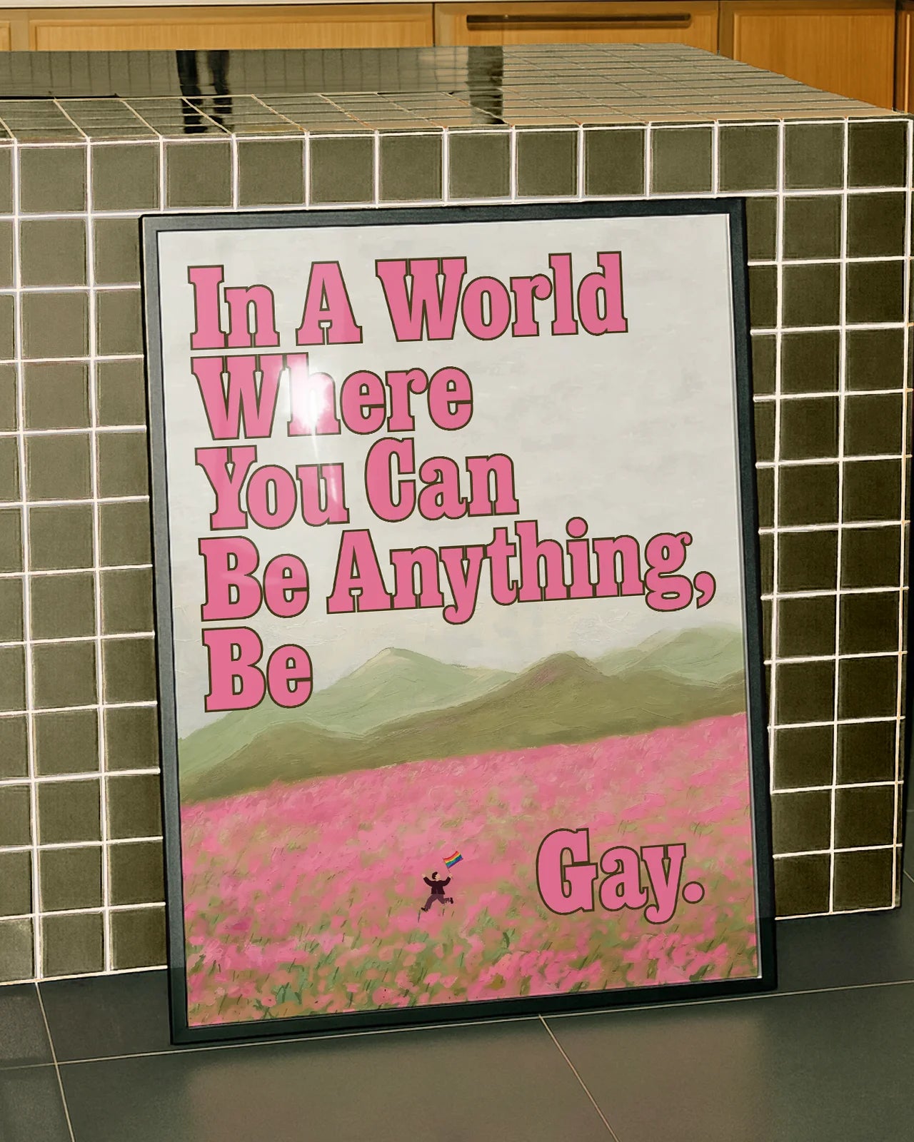 A poster of a person running through an open field of pink flowers, with a pride flag and the text: 'In a world where you can be anything, be gay'.