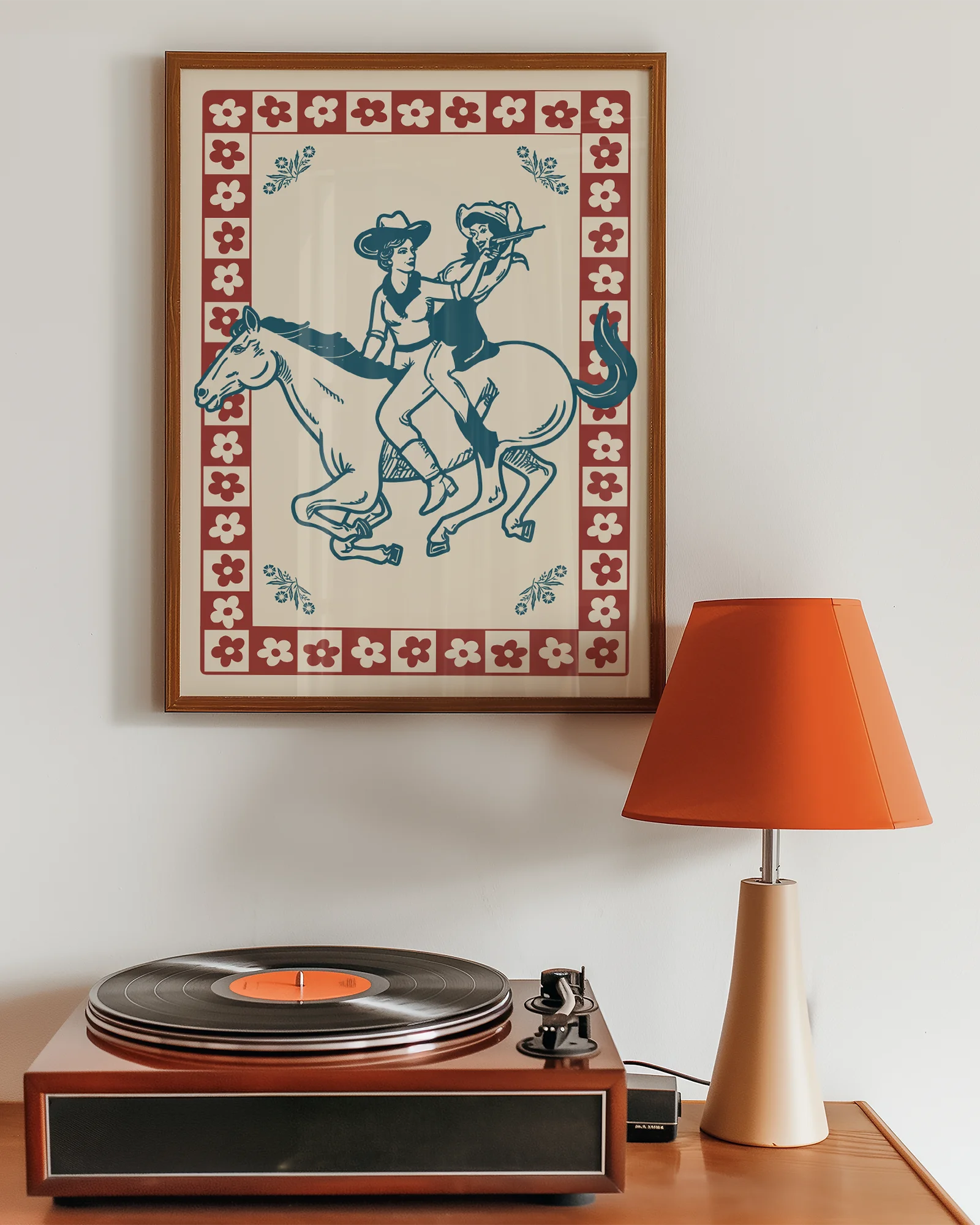 A framed poster featuring two cowgirls riding a horse, surrounded by a retro-style floral frame.
