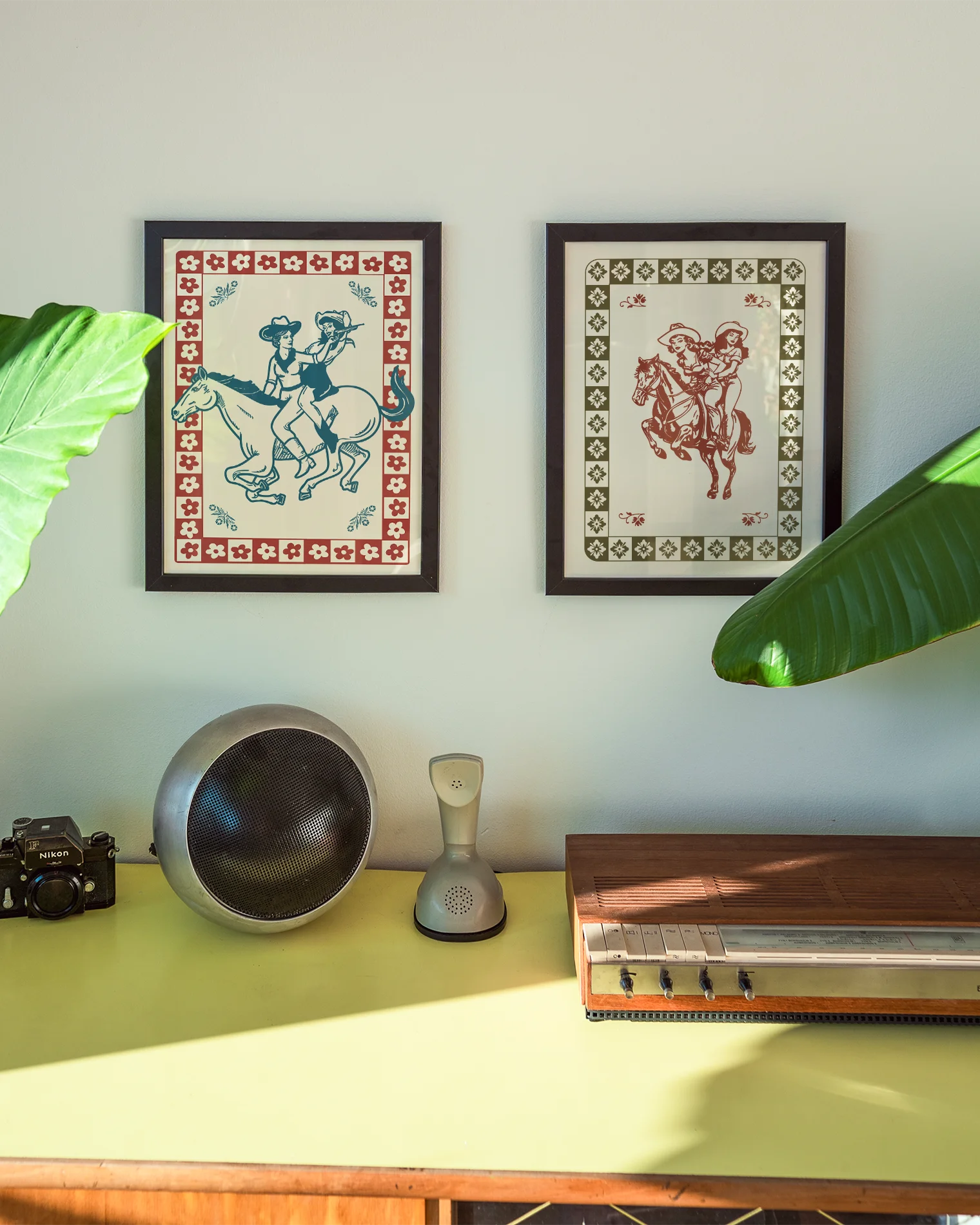 A framed poster featuring two cowgirls riding a horse, surrounded by a retro-style floral frame.