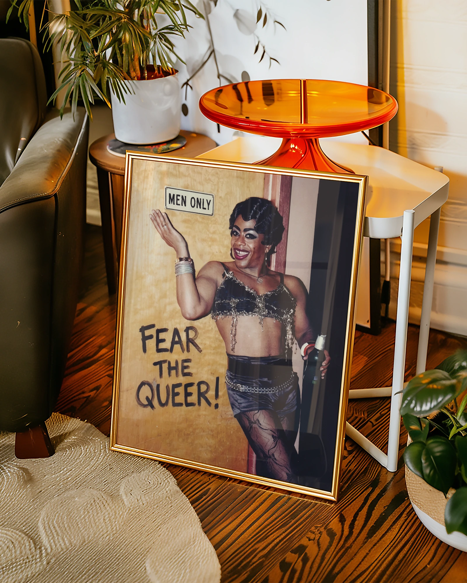 A framed poster with a black drag queen standing in front of a wall with a sign 'MEN ONLY', smiling.