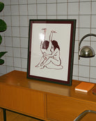 A framed print with two naked girls, hugging tight on the floor.