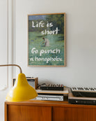 En postern som föreställer en kvinna som plockar blommor i ett öppet fält, i en klassisk oljemålnings-stil med texten 'Life is short Go punch a homophobe".