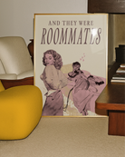 A framed poster depicting a woman lying in bed, and another woman undressing to join her — with the text “AND THEY WERE ROOMMATES.”