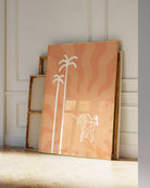 A print with an illustrated lesbian, baked couple dancing under a red sun and palms.