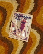 A poster with a lady coming home to her wife, who's in the bed with her legs up in the air with the text 'Welcome home baby!'. Sapphic, vintage style.
